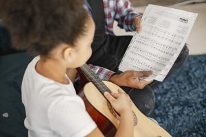 father-with-daughter-couch-girl-holding-guitar-learning-guitar_1157-47340